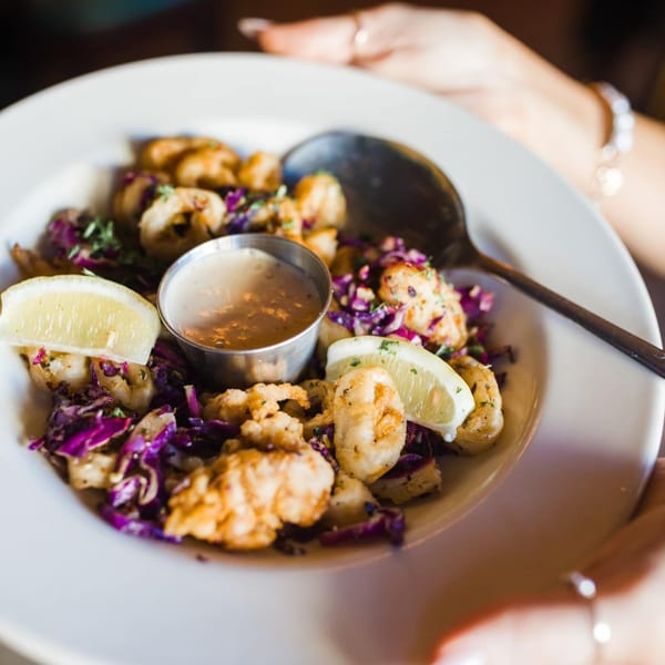 Crispy fried calamari with purple cabbage, lemon wedges, and a side of dipping sauce.