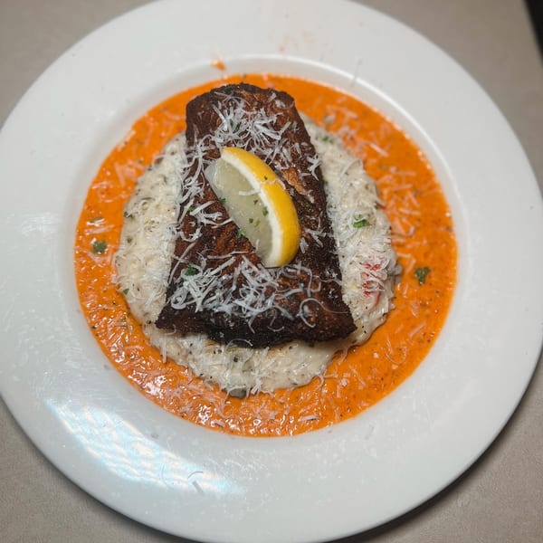 Blackened fish with lemon on creamy risotto, surrounded by orange sauce and grated cheese.
