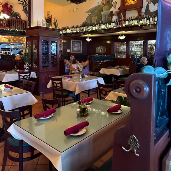 An Italian Kitchen dining room with tables set, patrons dining, and wine bottles lining the walls.