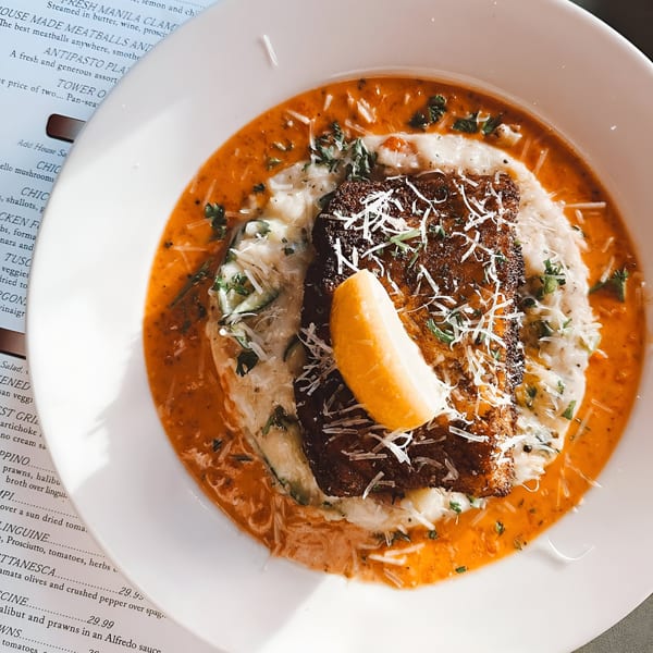 Italian Kitchen's pan-seared fish with risotto, red sauce, parmesan, and a lemon wedge.