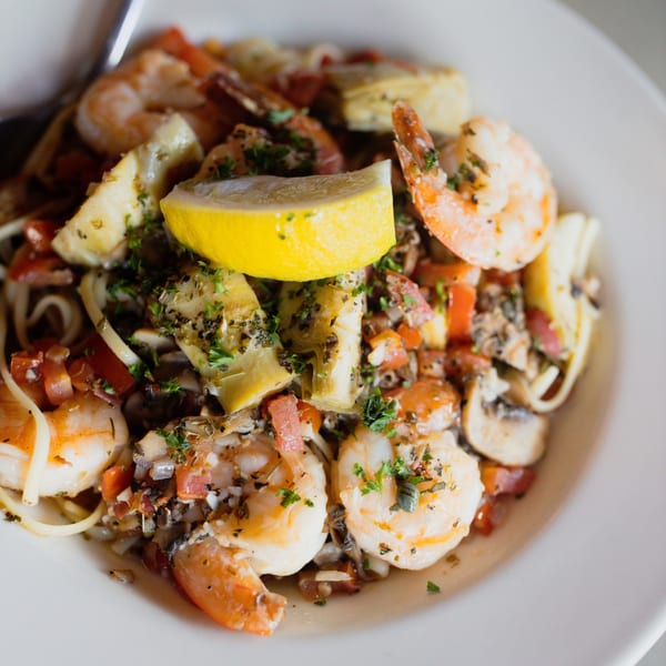 Italian Kitchen's shrimp scampi with pasta, artichokes, tomatoes, mushrooms, and a lemon wedge.