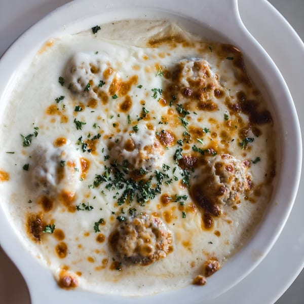 Baked Italian meatballs in a creamy white sauce, topped with melted cheese and fresh parsley.