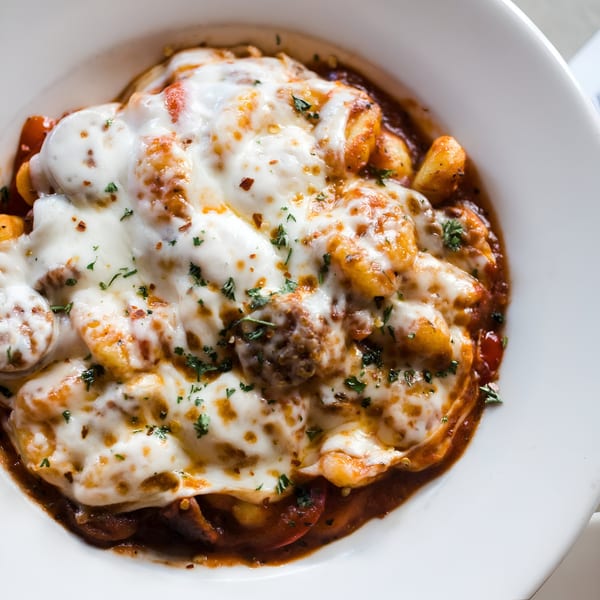 A white bowl filled with Italian gnocchi, meatballs, and melted cheese, garnished with parsley.