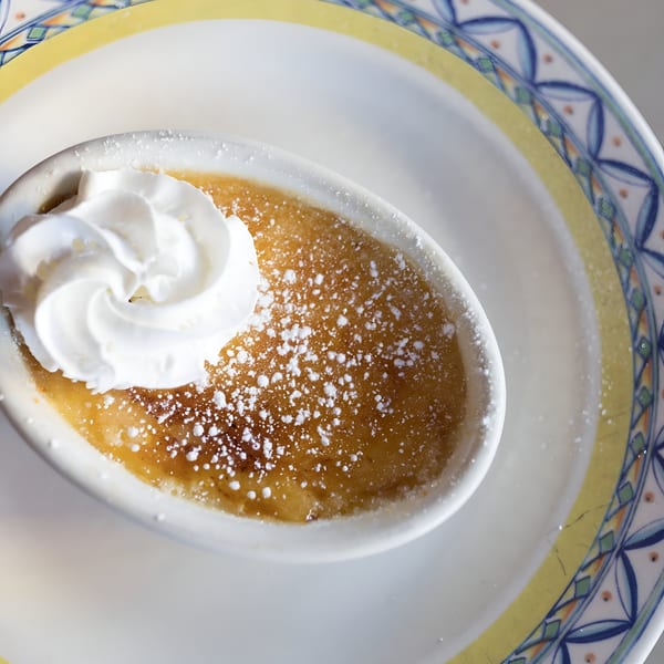 A creme brulee dessert with whipped cream and powdered sugar on a decorative plate.