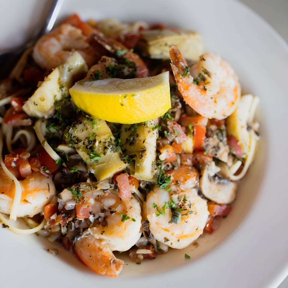 Shrimp scampi with linguine, artichoke hearts, diced tomatoes, mushrooms, and a lemon wedge.