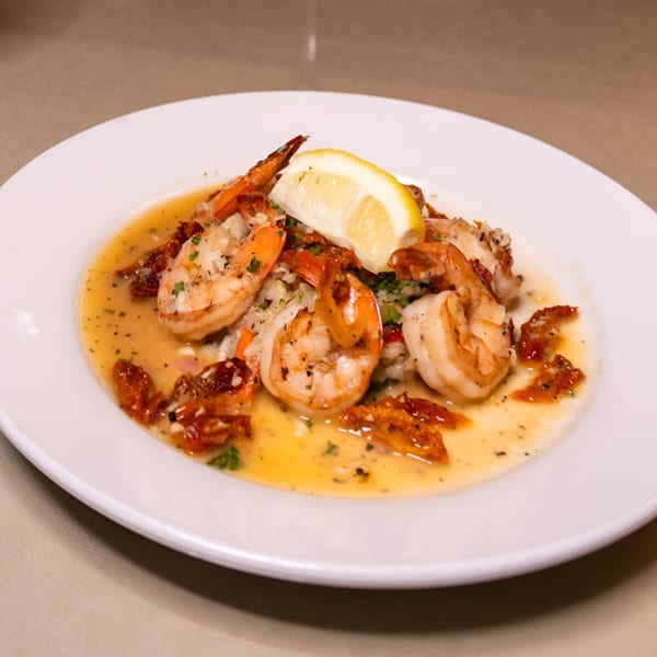 Italian Kitchen's shrimp scampi with sun-dried tomatoes, herbs, and a lemon wedge on a white plate.